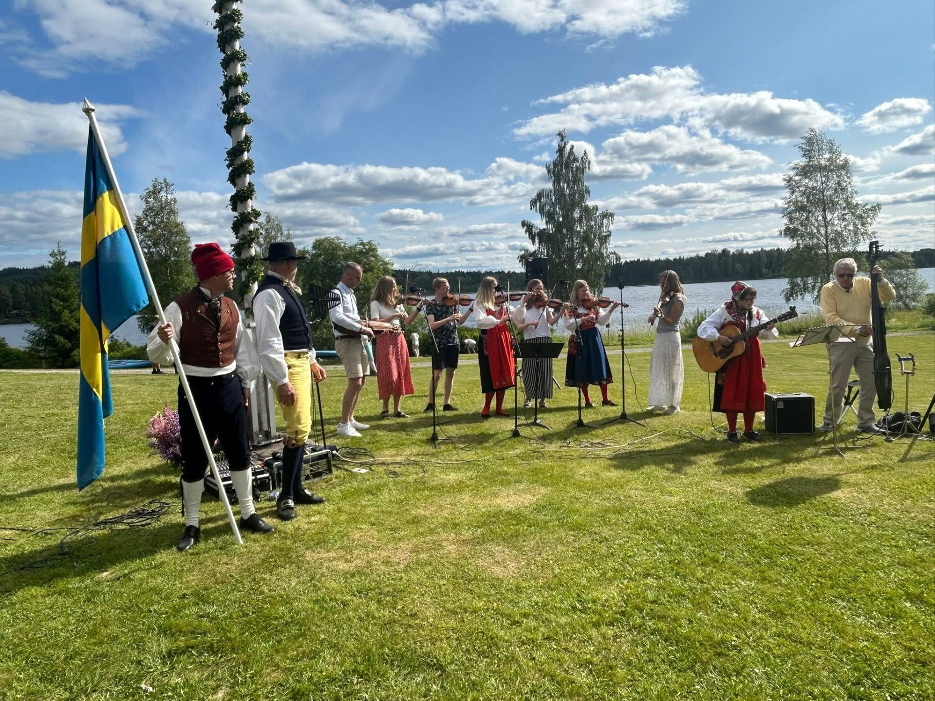 Spelmän i folkdräkt spelar vid midsommarstången på Dalagården
